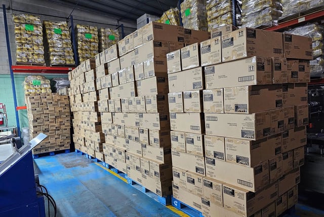 Hileras de cajas cerradas acomodadas sobre tarimas en un área interior